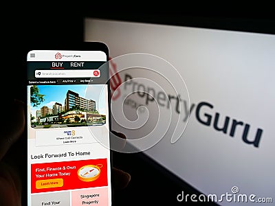 Person holding smartphone with website of online property company PropertyGuru Pte. Ltd. on screen with logo. Editorial Stock Photo