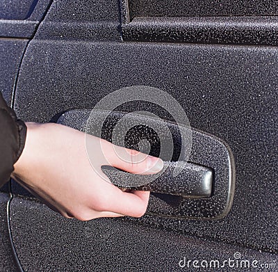 A person holds a frozen car handle in winter. A man opens the door in a black car covered in hoarfrost morning frosts. Stock Photo