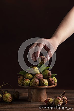 A person holds a lychee in his hand, on a dark background,Litchi chinensis Sonn,lizhi,close up Stock Photo