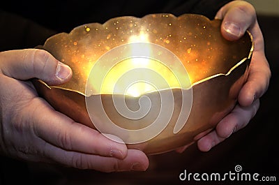 A person holds a magic bowl in his hands, from which a magical light shines Stock Photo