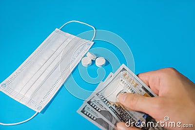 Person holds money in hand near a medical mask and medication. It symbolizes the purchase of medicines, the cost of treatment Stock Photo