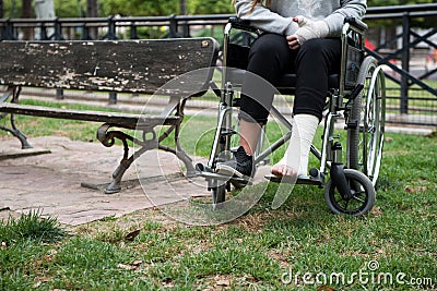 Person injured in a wheelchair. Foot and hand bandages, outdoor photography in a park Stock Photo
