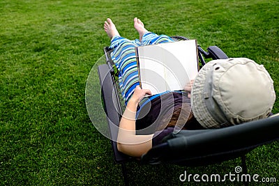 Person Lounging in Lawn Chair Relaxing and Reading Book Stock Photo
