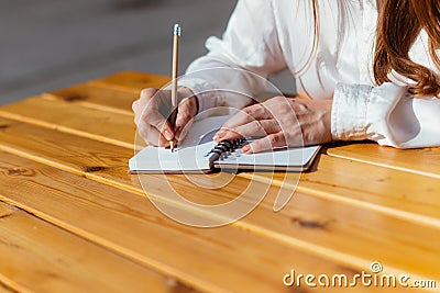 Person makes notes with a pencil in a notebook while sitting in a cafe in the summer on the street Stock Photo