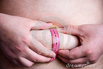 Person or patient measures by himself thickness of fat skin folds for presence of subcutaneous fat using measuring tape on his bel Stock Photo