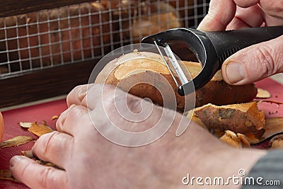 Person peeling fresh raw sweet potato with a vegetable Stock Photo