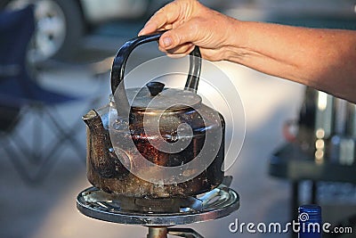 A PERSON PLACING A BLACKENED WATER KETTLE ONTO A GAS PLATE Stock Photo