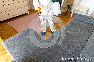 Person in protective suit with decontamination sprayer bottle disinfecting household and furniture Stock Photo