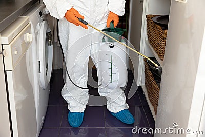 Person in protective suit with decontamination sprayer bottle disinfecting kitchen. COVID-19 pandemic concept Stock Photo