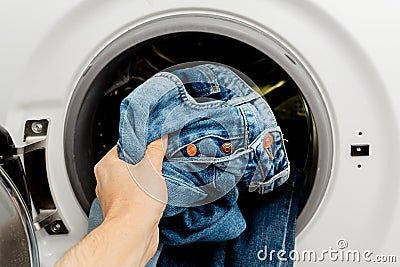 Person putting jeans into the drum of a washing machine, front view. Washing dirty jeans Stock Photo