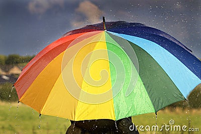A person with rainbow colored umbrella in the rain Stock Photo