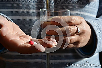 Person with red & white capsule and glass of fresh water Stock Photo