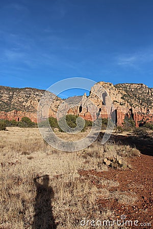 A person's shadow cast on a prairie like plateau on the Brins Mesa Trail lined by mountaintops in Arizona Stock Photo