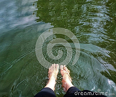 Person seated on a boulder in a lake, with their feet submerged in the cool, refreshing water Stock Photo