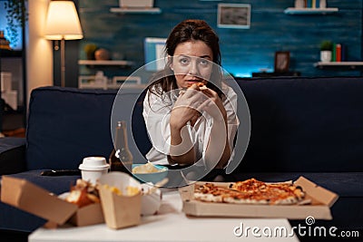 Person sitting on couch in living room having a slice of delivery pizza while watching television sitcom Stock Photo