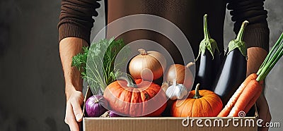 Person stands behind cardboard box on table, actively packing vegetables, orange pumpkins, purple eggplants, white Stock Photo