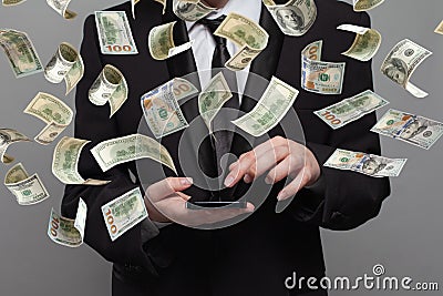 Person in suit works on mobile phone under money rain on grey background Stock Photo