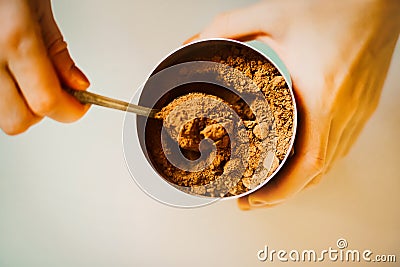 A person takes a teaspoon of a handful of natural fragrant cocoa powder from a jar Stock Photo