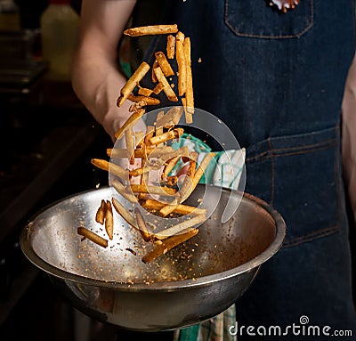 Person tossing freshly cooked fries with spices on a mixing bowl Stock Photo