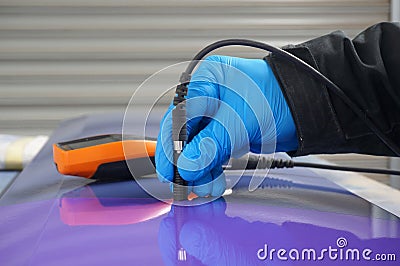 Person using probe, with digital tester, to measure the paint thickness microns on a painted metal panel. Stock Photo