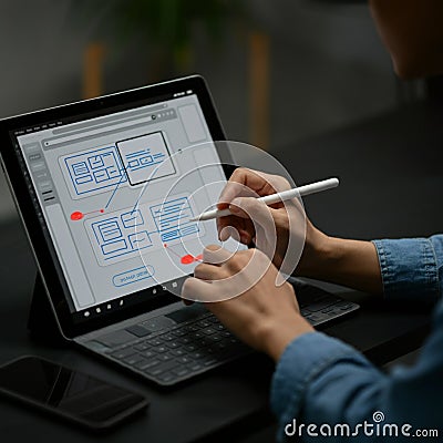 A person is using a stylus to create a digital wireframe on a tablet with a keyboard attached. Stock Photo
