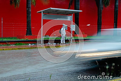 Person stands in the rain at bus stop while a car drives past him Stock Photo