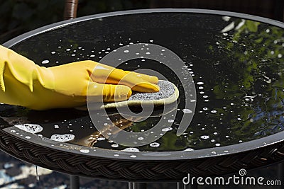 Person wearing rubber gloves cleaning a glass top patio table in a garden Stock Photo