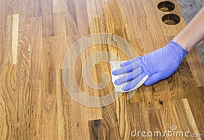 Person working rubbing oiling with linseed oil natural wooden kitchen countertop before using. Solid wood butcher block. Stock Photo