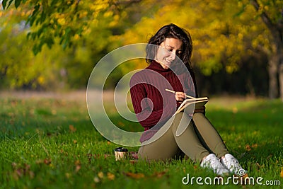 A person write notes sitting on a lawn in an autumn park. Joyful state of mind. Looking for inspiration Stock Photo