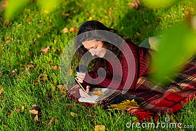 Person writes notes lying on the lawn in the autumn park. Solitude with yourself Stock Photo