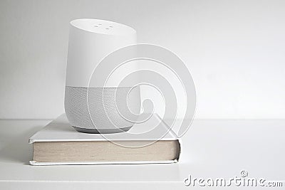 Personal assistant loudspeaker on a white wooden shelf of a smart home living room. Next, a book. Empty copy space Editorial Stock Photo