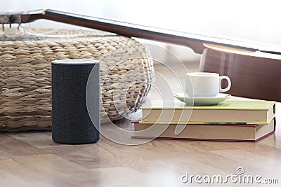 Personal assistant loudspeaker on a wooden floor of a smart home living room. Next, a guitar and some books and a cup of coffee. Stock Photo