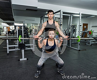Personal trainer helping work with barbell in gym Stock Photo