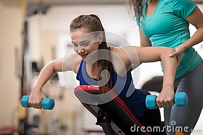 Personal trainer helping young woman with weight training equipment in gym Stock Photo