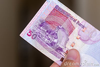 Persons hand giving the Currency of the Qatar - One fifty rial or riyal note spread out on a brown background. Money exchange Stock Photo