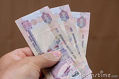 Persons hand giving the Currency of the United Arab Emirates UAE - Five hundred Dirham notes spread out on a brown background. Stock Photo