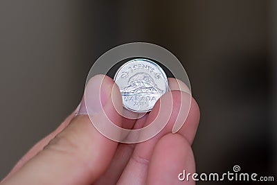 Persons hand holding out a nickle coin or five cents, the Currency of the Canada - on a brown background. Money exchange Editorial Stock Photo