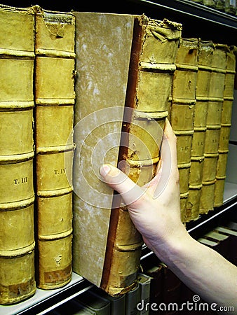 Persons hand removing old book from bookshelf Stock Photo