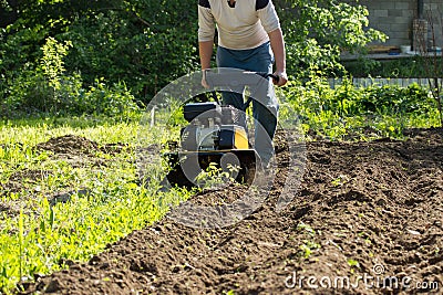 Perspective view of man plowing garden soil by motor cultivator Stock Photo