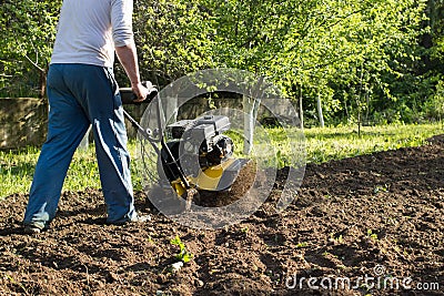 A perspective view of a man during soil plow process by motor cultivator Stock Photo