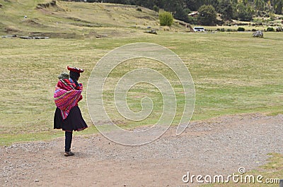 Peru,Cusco.Indigenous woman with baby in the back walking in field of SasayhuamÃ¡n, ancient military fortress of the Inca Editorial Stock Photo