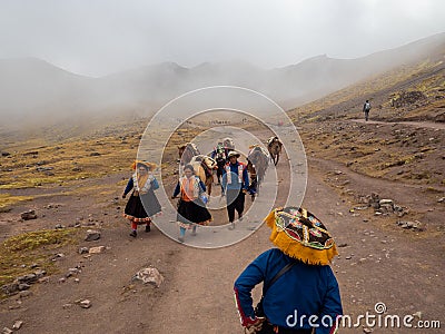 Natives with horses walk down dirt road dressed with colorful traditional clothes, fog Editorial Stock Photo