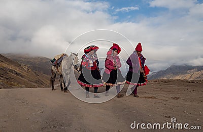 Three native women walk and talk leading a horse as they walk on a dirt road wearing Editorial Stock Photo