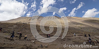 Tourists walk down dirt path next to mountain range under blue sky Editorial Stock Photo