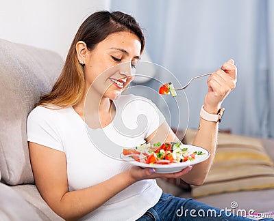 Peruvian housewoman eating vegetable salad on sofa at home Stock Photo