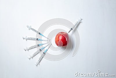 Pesticides and nitrates are injected into a red and green apple with a syringe. Gmo concept and genetically modified Stock Photo