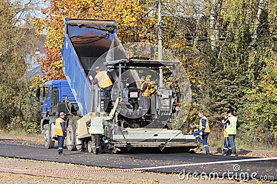 Heavy truck with body raise pours asphalt into an asphalt paver Editorial Stock Photo