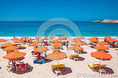 PETANI beach, Greece - July 21, 2020: People relaxing, yellow sunbeds, orange umbrellas, white sand, azure water. Editorial Stock Photo