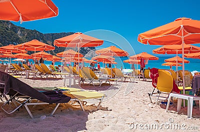 PETANI beach, Greece - July 21, 2020: Yellow sunbeds, orange umbrellas, white sand, azure water of Petani beach. Editorial Stock Photo