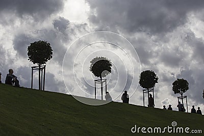 Row of manicured Tilia trees in line on and people walking on green grass lawn hill of Garden of Venus with blue sky Editorial Stock Photo